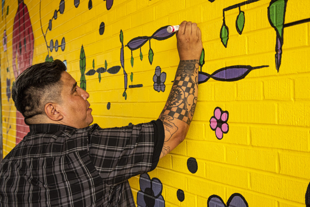 Les Harper touches up Two Worlds, a community mural project at The Bickford Centre in Toronto. The centre of the piece is an outline of a syringe, swaddled in purple. This colour represents the deadly opioid fentanyl. Photo by Declan Keogh.